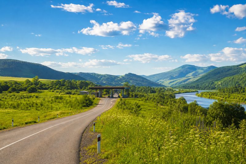 Country road winding through a sunlit valley toward a border crossing on the EU eastern land border